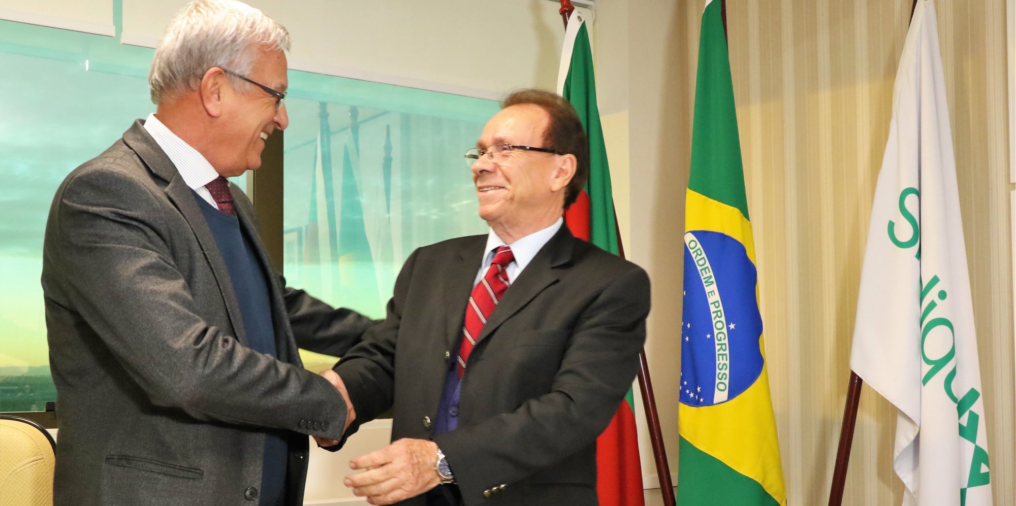 Dois homens dando um aperto de mãos em comemoração. Três bandeiras ao lado direito