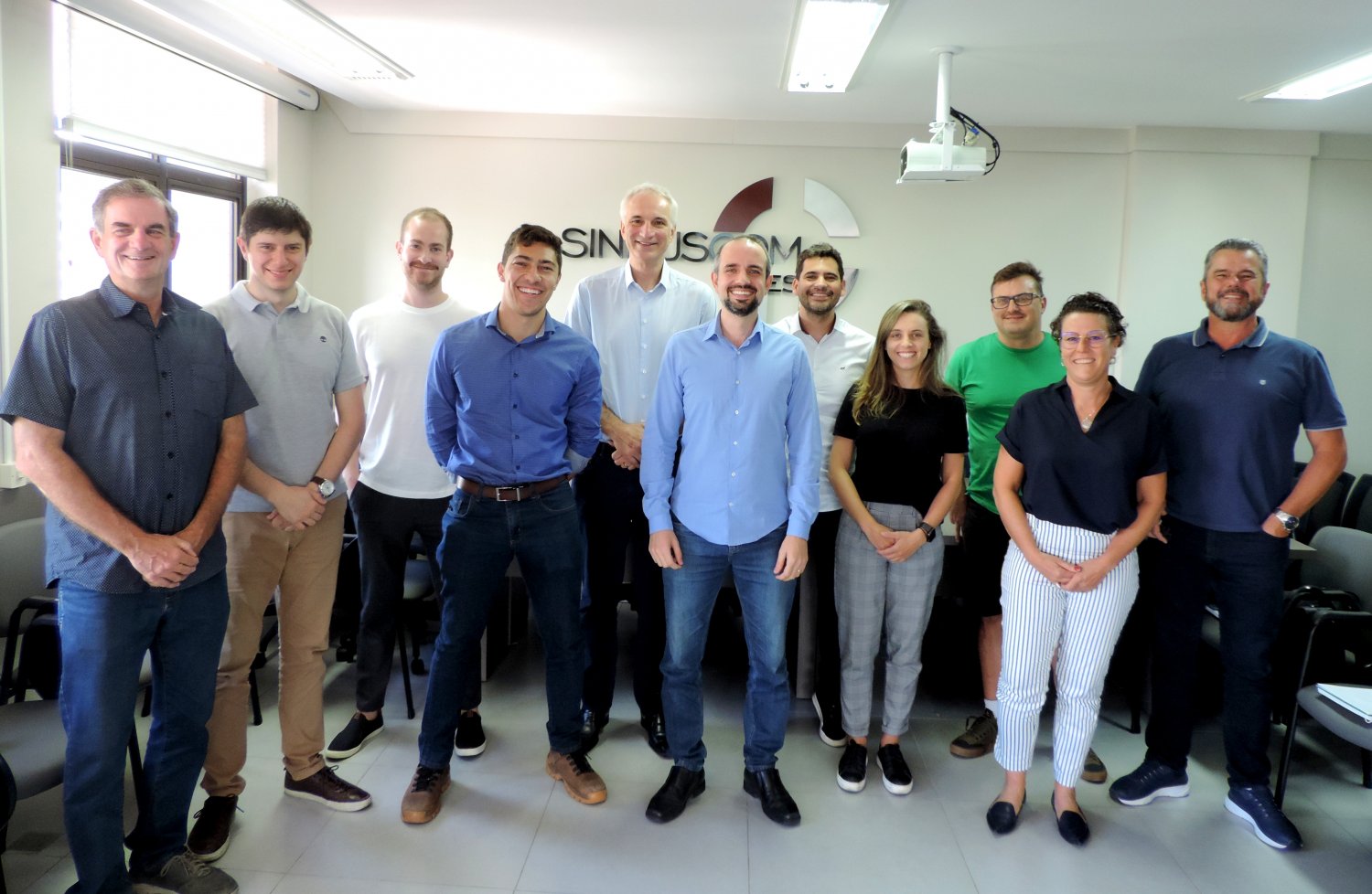 Homens e mulheres posicionados em frente ao Banner do Sinduscom Vales